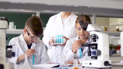 education, science and children concept - teacher and students with test tubes studying chemistry at school laboratory