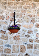 Violets in a decorative pot hang with a stone wall of the house