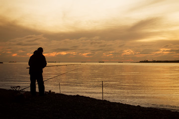 Fisherman on a sea coast and majestic sunset over water.