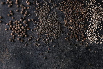 Variety of different black peppers allspice, pimento, monks pepper, peppercorns over old black iron...