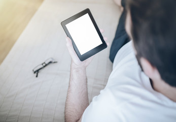 man relaxing on couch using e-book reader or small tablet computer