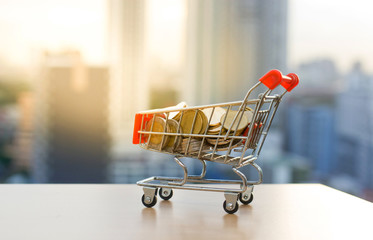 Shopping cart with coins on the table with blur building sunset background.Business concept.
