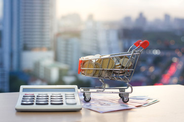 Shopping cart with gold coins Banknotes and calculator on the table with blur building background. Business concept. © Thannaree