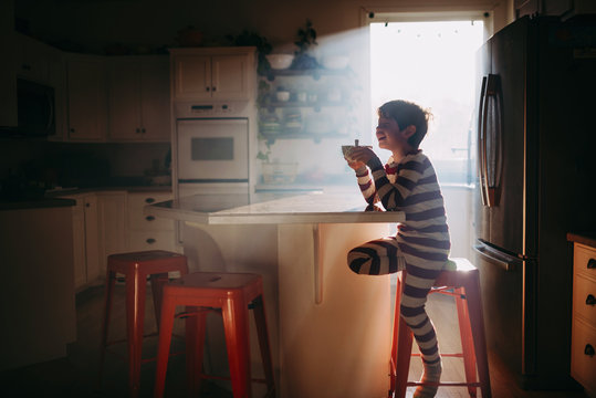 Boy sitting in kitchen eating his breakfast in morning light