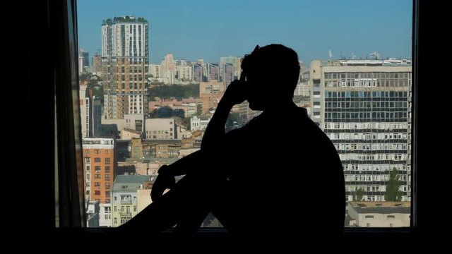 silhouette of a frustrated guy sitting on a window in high floor