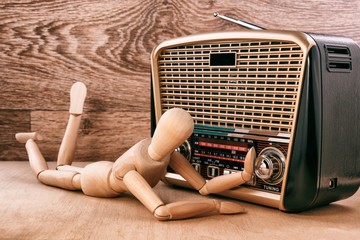 Wooden doll enjoy listening to music while lying near the radio receiver. Wooden background
