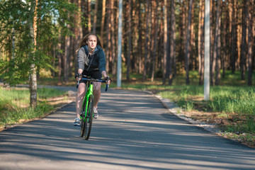 Girl on a bicycle in a grey hoodie in the park. Races on a bicycle. Active way of life and playing sports.	