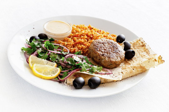 Turkey Cutlet With Bulgur Pilaf, Flat Bread, Parsley Onion Salad Decorated With Lemon And Olives Served With Adjika Yogurt Based Sauce