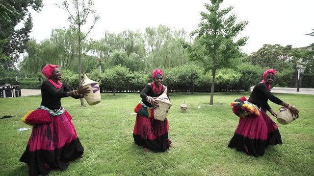 African women are dancing a folk traditional dance on a grass meadow, in traditional costumes with wicker baskets, sunny, trees' background, African costumes, traditions, African culture, tribes
