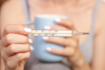 Woman sitting with a mug of tea and thermometer in hands hot healthy care