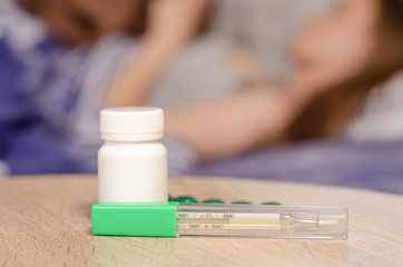 Obraz na płótnie Canvas Woman lies in bed sick with thermometer jar of pills medicine flu virus temperature