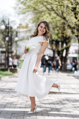 Naklejka premium The charming bride keeps a wedding bouquet and stands on the street