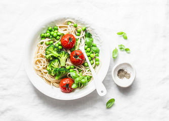 Simple veggie pasta. Vegetarian pasta spaghetti with broccoli cabbage, green peas and cherry tomatoes on light background, top view