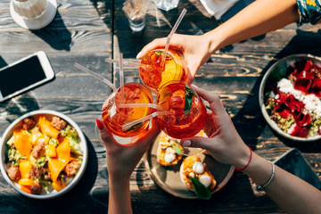 Overhead view of three women making a celebratory toast with aperol spritz cocktails