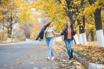 Fototapeta premium Young pretty girls having fun outdoors in autumn background. Cheerful friends in the fall time