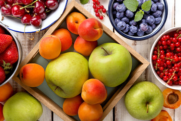 Various fresh ripe fruit on a wooden background. Apple, apricot, blueberry, cherry, strawberry, red currant viewed from above. Top view