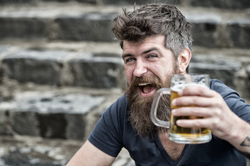 Hipster with long beard looks relaxed. Bearded hipster holds beer mug, drinks beer outdoor. Man...