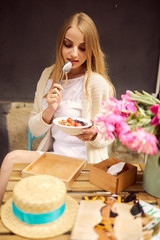 Pretty blonde girl eat her morning smoothie with flowers on the table
