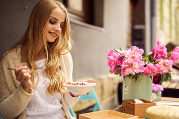 Obraz na płótnie Canvas Pretty blonde girl eat her morning smoothie with flowers on the table