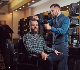 Professional barber working with a client in a hairdressing salon, uses a hair dryer.