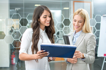Brunette and blonde business woman discussing document on clipboard in office