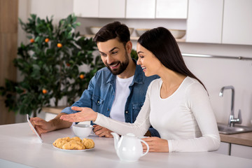 Obraz na płótnie Canvas Positive couple using tablet in the kitchen