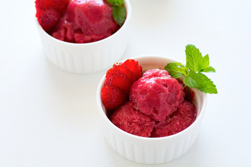 Fruit strawberry sorbet with mint in bowl on white wooden background.