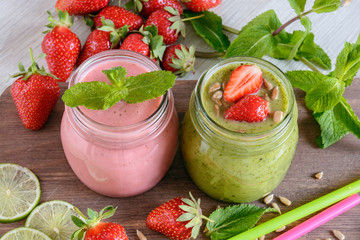 Two jar of bright smoothies surrounded by strawberries and mint stand on a table 