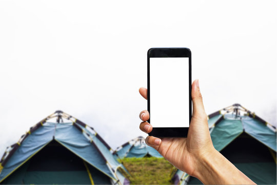 Hand holding black smartphone with white screen for mock up on camping tent as background.