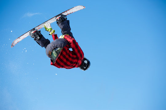 Photo from below of jumping man with snowboard and blue clear sky