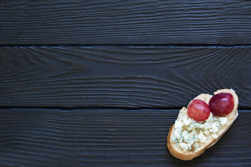 Bruschetta with  pink grapes and blue cheese on the black rustic wooden  background. Italian cuisine, top view. Copy space. Vegetarian.
