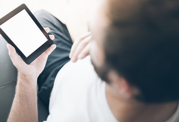 over the shoulder view of man sitting on armchair using e-book reader or small tablet computer