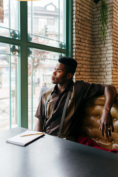 Black man sitting in cafe and writing looking through the window