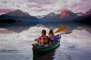 People on kayak paddling into serene beautiful lake with perfect reflection of mountains during summer sunset