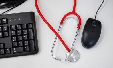 red stethoscope with black keyboard and mouse on white office desk