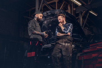 Obraz na płótnie Canvas Two mechanics talking during repairs a broken car in a garage.