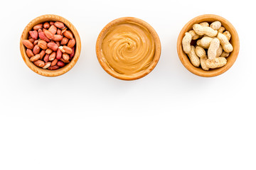 Peanut paste concept. Bowls with butter, nuts in shell, peeled nuts on white background top view copy space