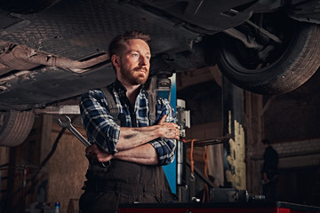 Fototapeta na wymiar Mechanic crossed hands while standing under lifting car in a repair garage.