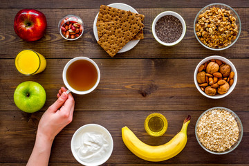 Fototapeta na wymiar Set of products for healthy vegetarian breakfast. Fruits, oatmeal, yogurt, nuts, crispbreads, chia on dark wooden background top view space for text. Hand takes tea
