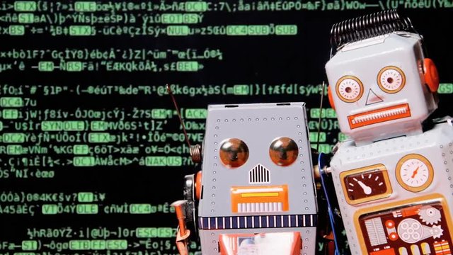 Two tin toy robots standing still in front of a screen showing encrypted scrolling source code. Room for copyspace on the left.
