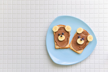children sandwiches with chocolate nut paste and bananas in the form of bear, lie on a plate on a table