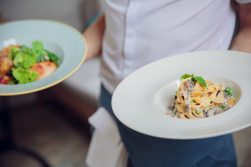Close up hand of the waiter is serving Spaghetti with creamy Sauce in the restaurant