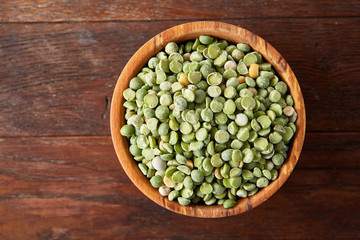 Organic green peas in a bowl on rustic wooden background, close-up, top view, selective focus.