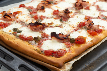 Homemade pizza with ham, mozzarella, tomato sauce, capers and oregano 