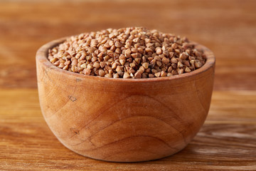 Bowl full of buckwheat grains on rustic wooden table, close-up, selective focus, shallow depth of field.
