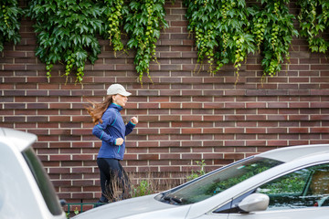 Young woman jogging along the street in eurpean city in the morning. Running fitness girl against brick wall