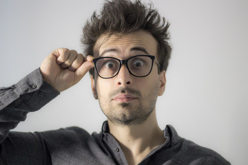 Puzzled emotional male with surprised expression looks through spectacles, tries to make out...