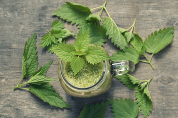 Fresh green smoothie with wild nettle and other herbs in mason jar on rustic wooden background....