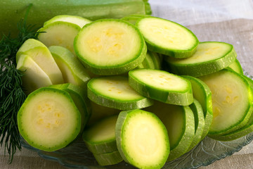 Sliced zucchini slices of a round shape with dill, laid on a glass plate for further preparation in...