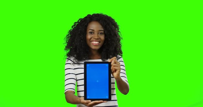 Pretty african american young curly woman in the striped blouse smiling and posing with a tablet device in hands on the chroma key background. Green screen. Tracking motion